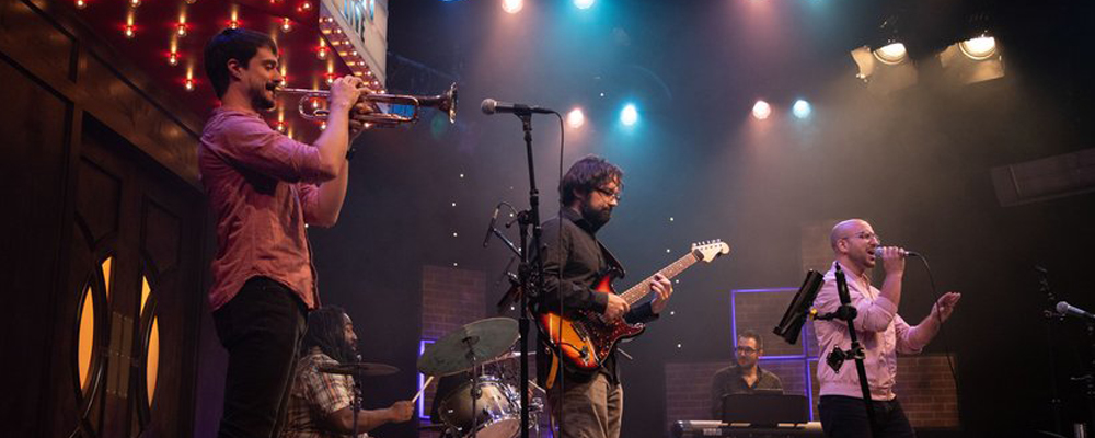 Band members on stage playing guitar, trumpet, and singing