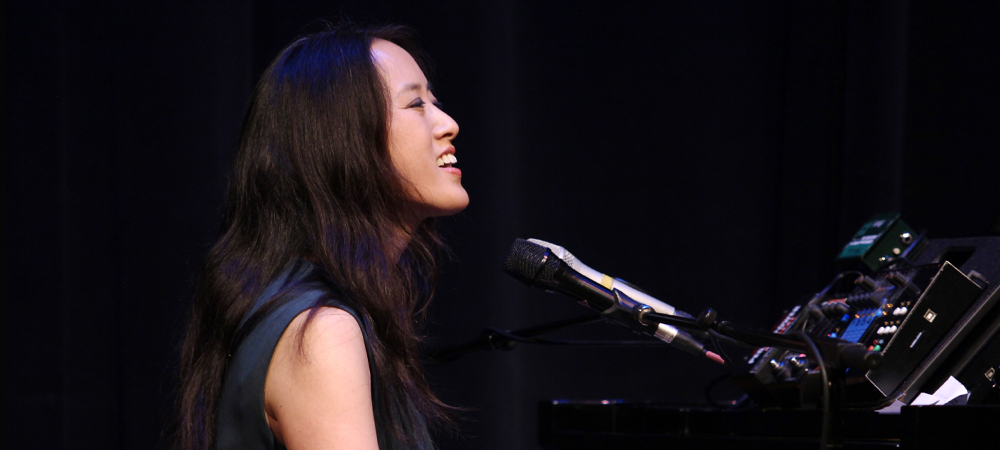 Female singing into microphone at a piano