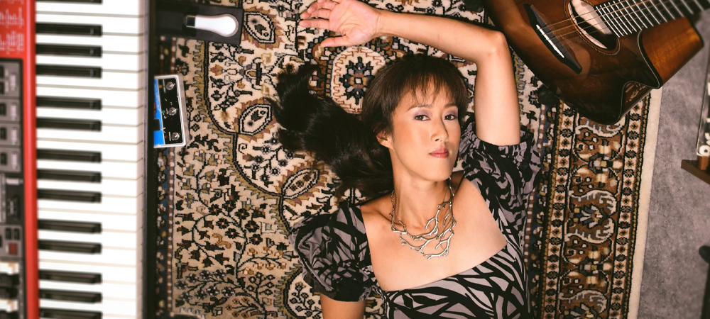 Artist Vienna Tang laying on a patterned rug with a guitar and keyboard