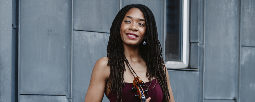Njioma Grevious in burgundy dress smiling with violin