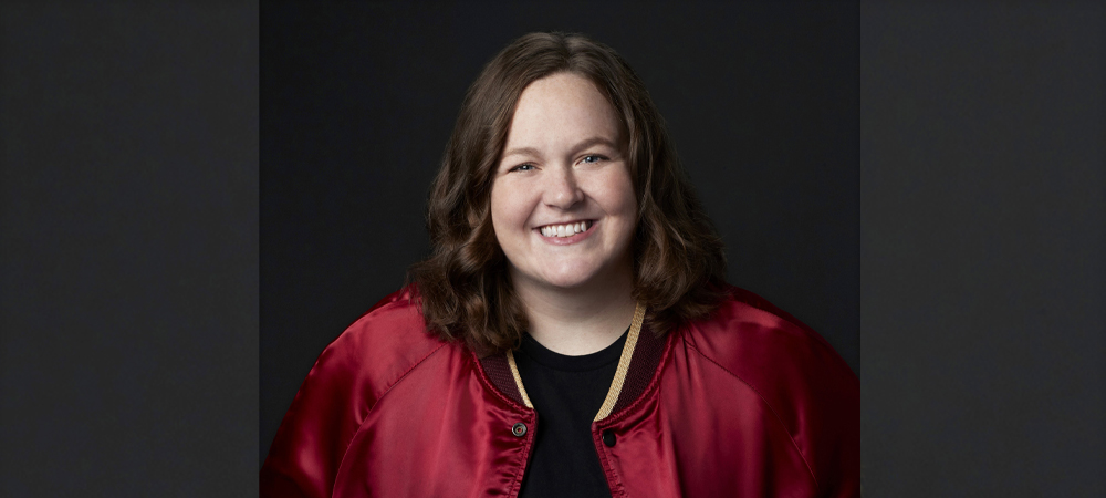 female with red jacket smiling in front of gray background